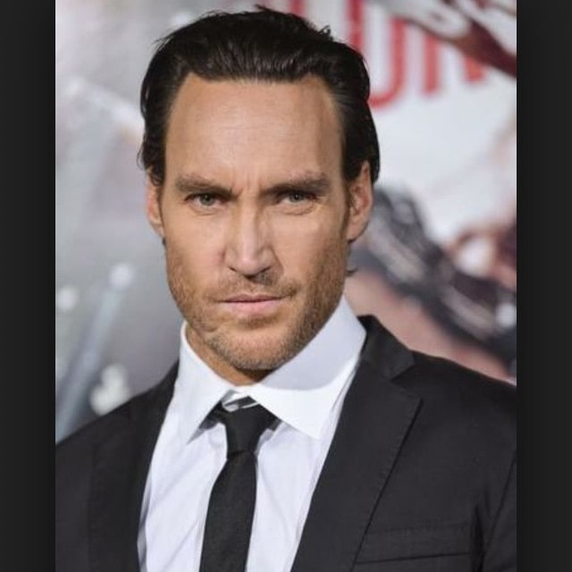 Callan Mulvey in a white shirt and black formal coat.